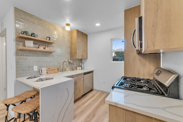 kitchen with light stone countertops, appliances with stainless steel finishes, a sink, light wood finished floors, and tasteful backsplash