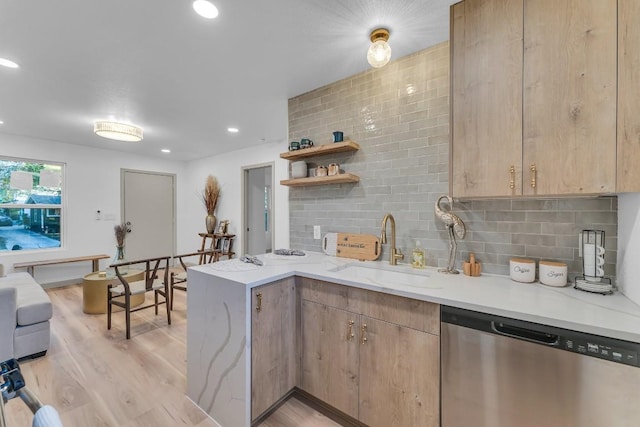 kitchen with a sink, light wood-style flooring, a peninsula, tasteful backsplash, and stainless steel dishwasher