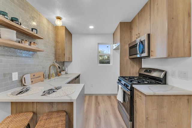 kitchen featuring appliances with stainless steel finishes, backsplash, sink, light hardwood / wood-style floors, and a breakfast bar area