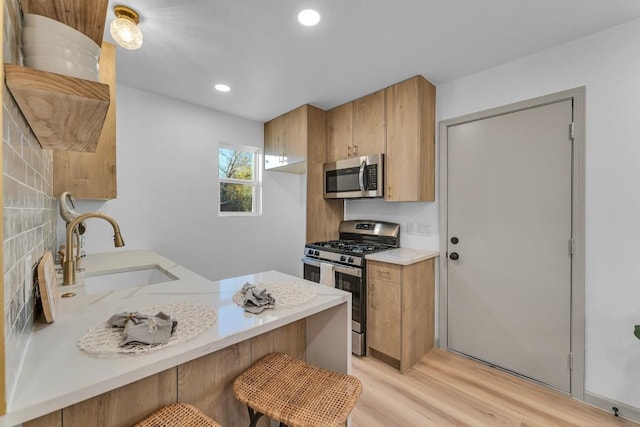 kitchen with sink, stainless steel appliances, kitchen peninsula, light hardwood / wood-style floors, and a breakfast bar area