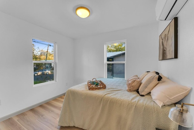 bedroom featuring light wood-style floors, baseboards, multiple windows, and a wall unit AC