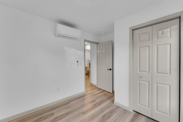 unfurnished bedroom featuring a closet, baseboards, a wall mounted AC, and light wood-type flooring