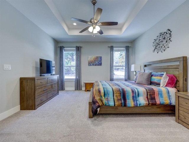 carpeted bedroom featuring ceiling fan, a raised ceiling, and multiple windows