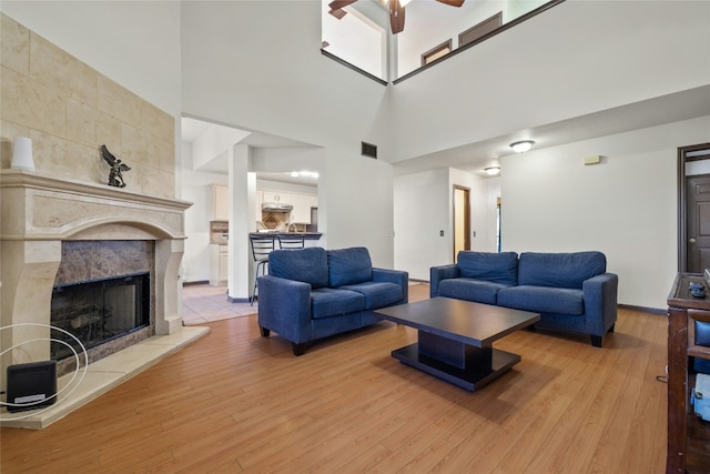 living room with ceiling fan, a towering ceiling, a fireplace, and light hardwood / wood-style flooring