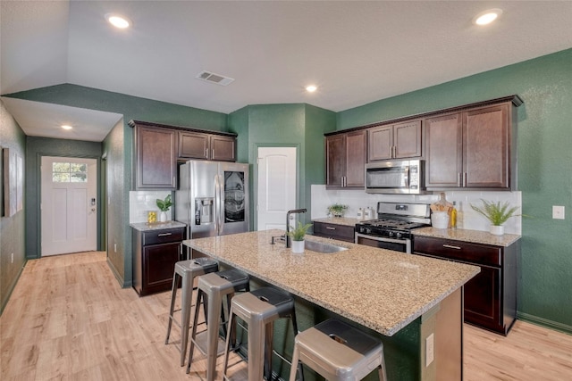 kitchen with appliances with stainless steel finishes, light stone counters, a breakfast bar, a kitchen island with sink, and sink