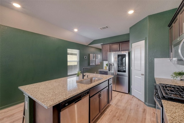 kitchen with dark brown cabinetry, sink, stainless steel appliances, vaulted ceiling, and a kitchen island with sink