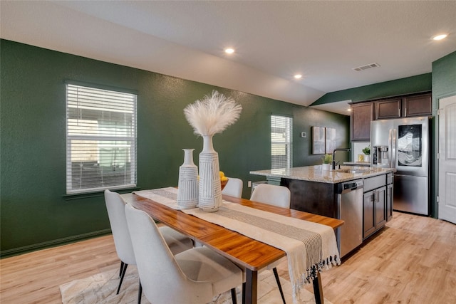 kitchen with light stone countertops, appliances with stainless steel finishes, dark brown cabinetry, lofted ceiling, and an island with sink