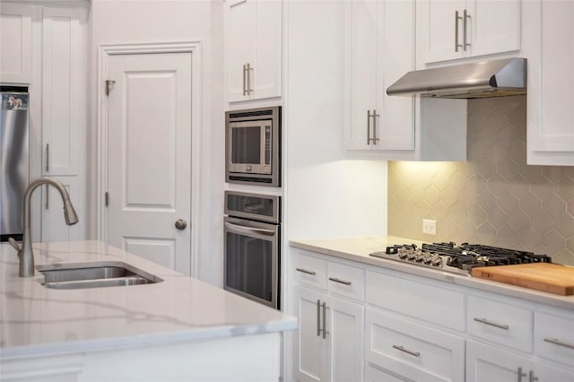 kitchen with light stone counters, stainless steel appliances, sink, and white cabinets