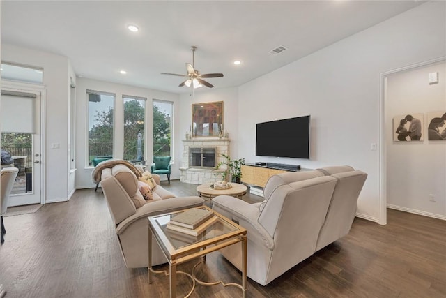 living room with dark wood-type flooring, ceiling fan, and a stone fireplace