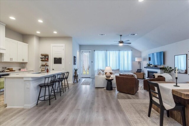 living room with ceiling fan, sink, vaulted ceiling, and light wood-type flooring