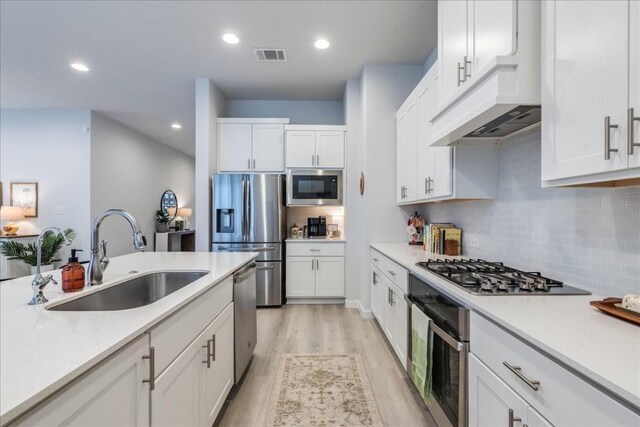 kitchen with appliances with stainless steel finishes, custom exhaust hood, sink, light hardwood / wood-style flooring, and white cabinetry