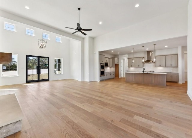 unfurnished living room featuring french doors, sink, ceiling fan, light wood-type flooring, and a towering ceiling