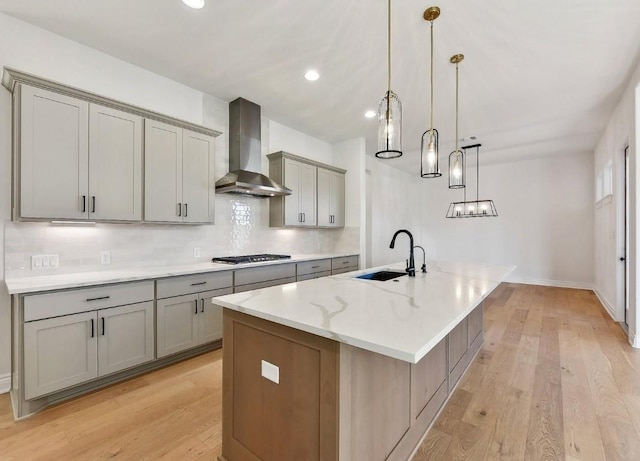 265 Gaucho Way, Dripping Springs, TX 78620 - kitchen featuring a sink, wall chimney exhaust hood, gray cabinetry, a center island with sink, and backsplash
