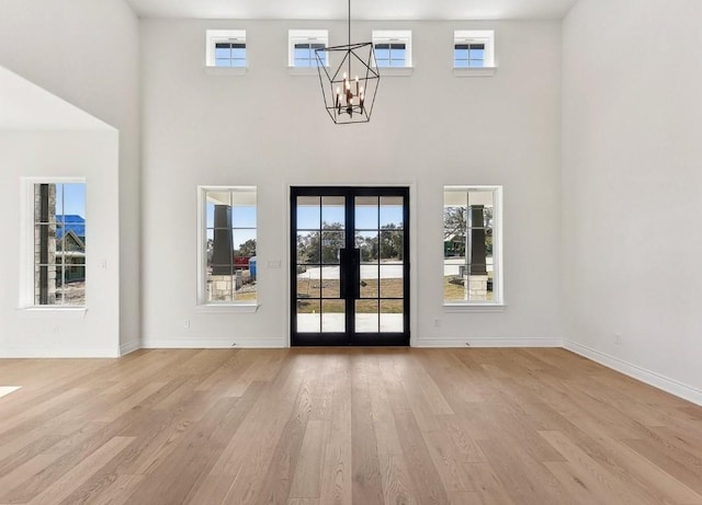 interior space featuring a towering ceiling, french doors, an inviting chandelier, and light hardwood / wood-style flooring