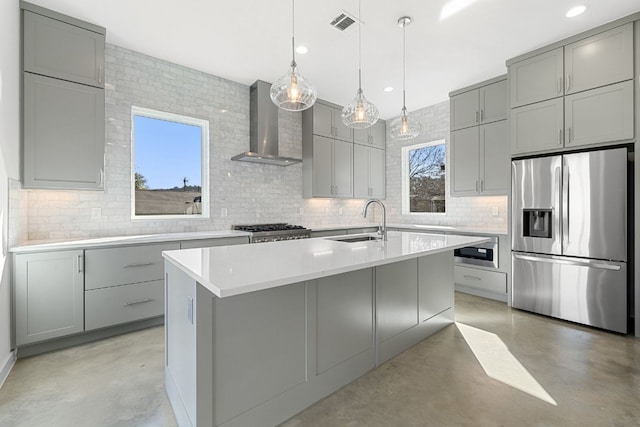 kitchen featuring stove, a center island with sink, sink, stainless steel refrigerator with ice dispenser, and wall chimney exhaust hood