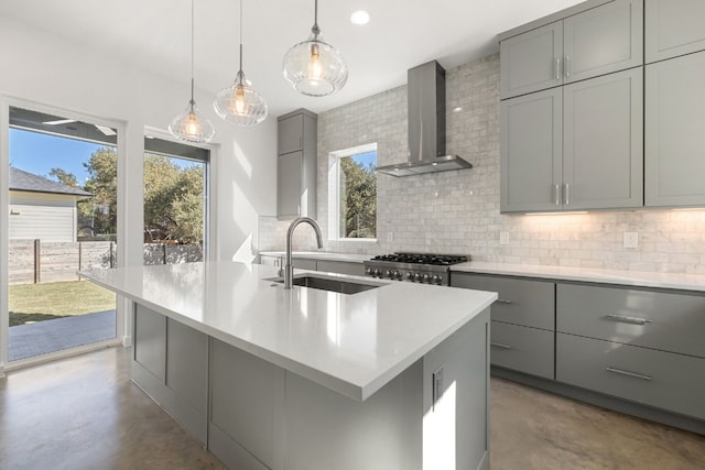 kitchen featuring sink, wall chimney exhaust hood, stove, gray cabinets, and a center island with sink