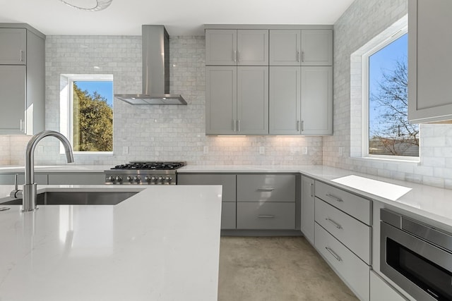 kitchen with a healthy amount of sunlight, built in microwave, gray cabinetry, and wall chimney range hood