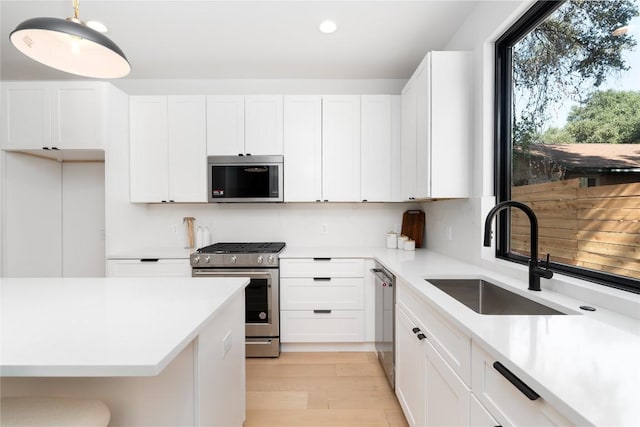 kitchen featuring white cabinets, sink, light wood-type flooring, decorative light fixtures, and stainless steel appliances