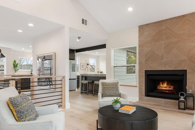 living room featuring sink, vaulted ceiling, light hardwood / wood-style flooring, and a tiled fireplace