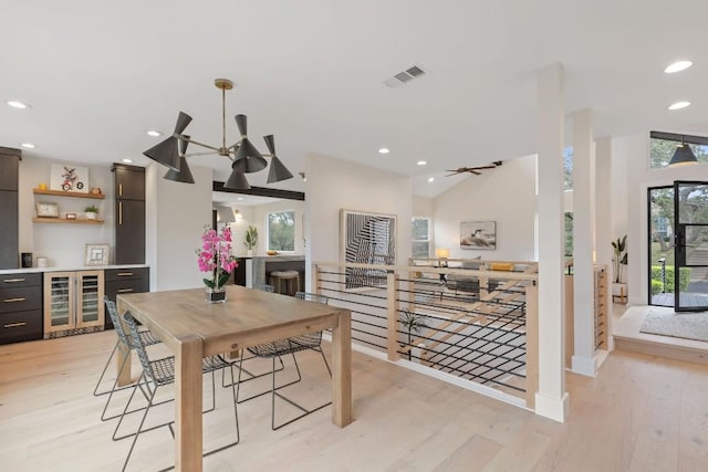 dining space with ceiling fan with notable chandelier, light wood-type flooring, wine cooler, and lofted ceiling