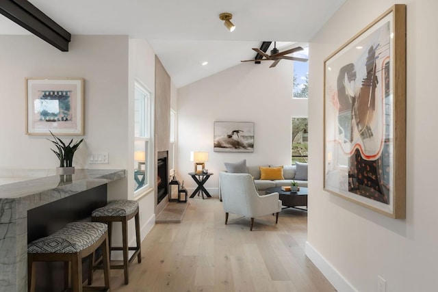 living area with ceiling fan, light hardwood / wood-style flooring, and lofted ceiling with beams