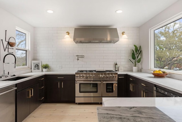 kitchen featuring backsplash, wall chimney range hood, sink, plenty of natural light, and stainless steel appliances