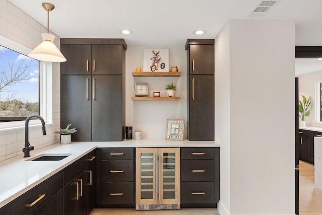 bar with pendant lighting, sink, tasteful backsplash, dark brown cabinets, and beverage cooler