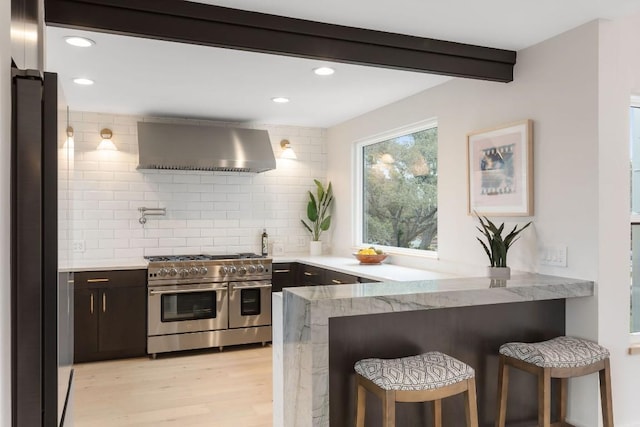 kitchen with wall chimney exhaust hood, appliances with stainless steel finishes, tasteful backsplash, kitchen peninsula, and a breakfast bar area