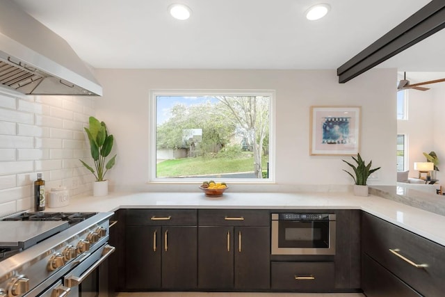 kitchen featuring dark brown cabinetry, wall chimney exhaust hood, wall oven, decorative backsplash, and high end stainless steel range