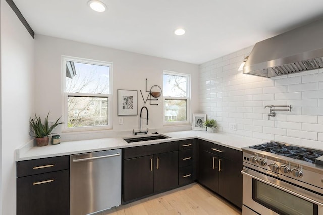 kitchen featuring sink, stainless steel appliances, wall chimney range hood, light hardwood / wood-style flooring, and decorative backsplash