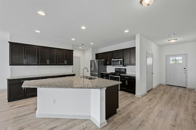 kitchen featuring sink, stainless steel appliances, tasteful backsplash, light stone counters, and a kitchen island with sink