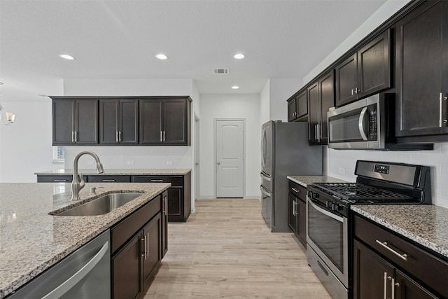 kitchen featuring sink, stainless steel appliances, light stone counters, decorative backsplash, and light wood-type flooring