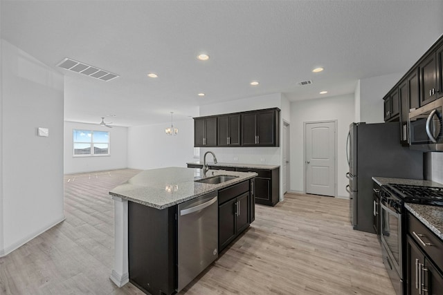 kitchen featuring light stone countertops, tasteful backsplash, stainless steel appliances, a kitchen island with sink, and sink