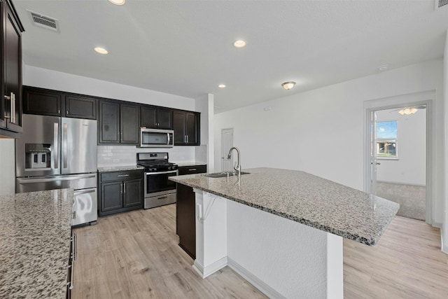 kitchen with light stone counters, sink, an island with sink, and stainless steel appliances