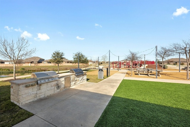 surrounding community with a lawn, a patio area, a water view, and an outdoor kitchen