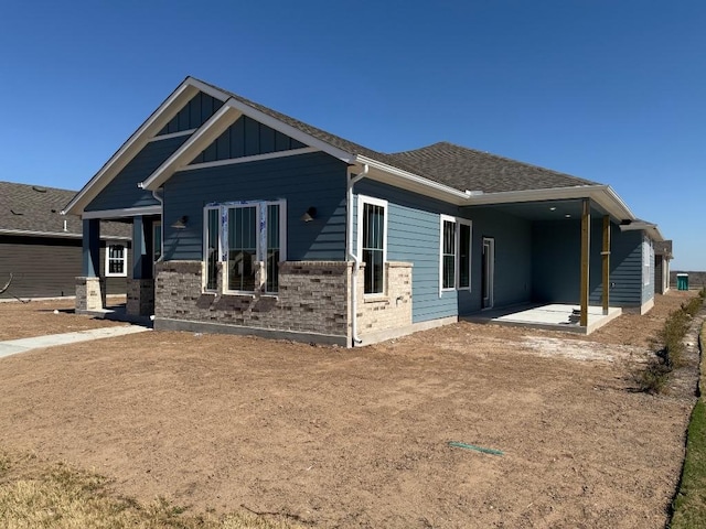 view of front of house featuring brick siding, board and batten siding, a shingled roof, and a patio