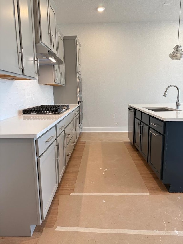 kitchen featuring gray cabinets, a sink, under cabinet range hood, tasteful backsplash, and appliances with stainless steel finishes