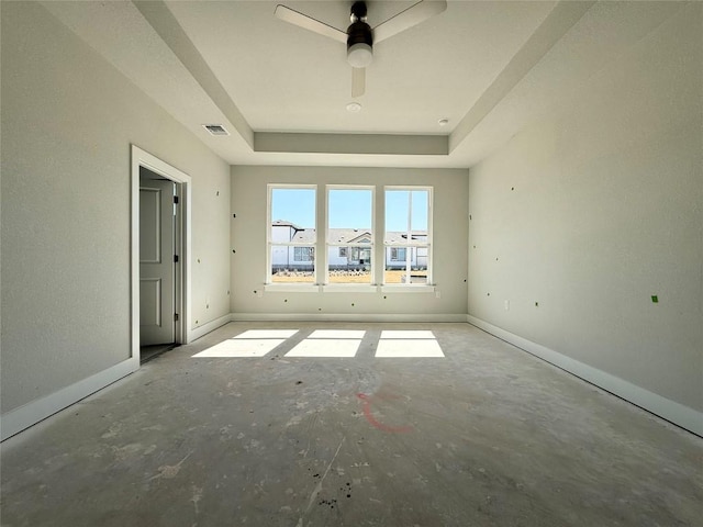 spare room with a tray ceiling, baseboards, visible vents, and ceiling fan