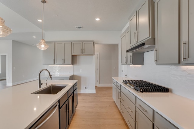 8504 Dongan Dr, Austin, TX 78744 - kitchen featuring under cabinet range hood, a sink, stainless steel gas cooktop, gray cabinetry, and dishwashing machine