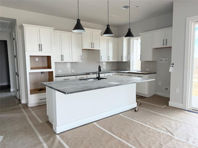 kitchen featuring decorative backsplash, white cabinetry, an island with sink, and a sink