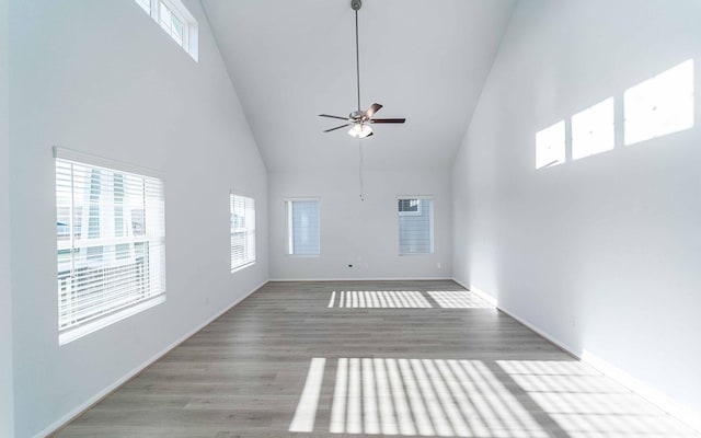 unfurnished living room with ceiling fan, a towering ceiling, and light wood-type flooring