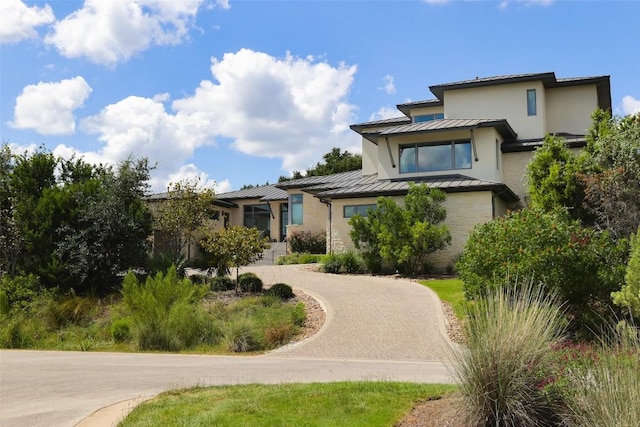 back of property featuring decorative driveway, a standing seam roof, and metal roof