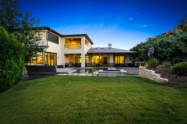 rear view of house with a yard, a swimming pool with hot tub, a balcony, and a patio