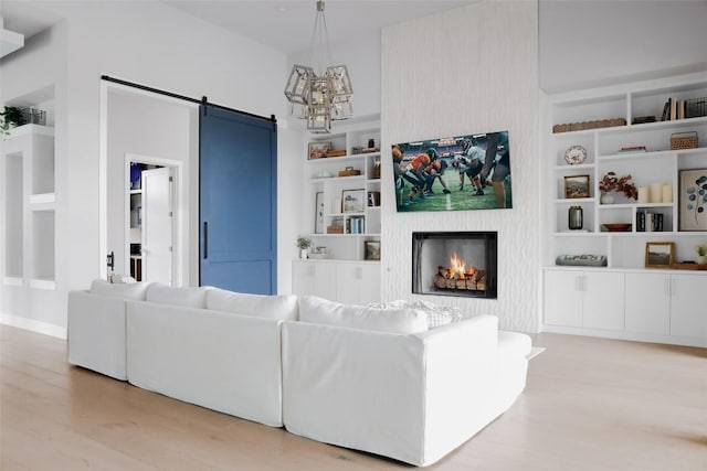 living room with a barn door, built in features, a notable chandelier, and light wood-type flooring