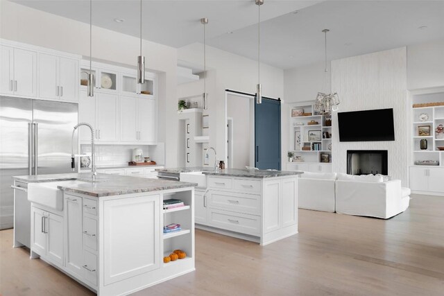 kitchen with a barn door, white cabinets, an island with sink, and hanging light fixtures