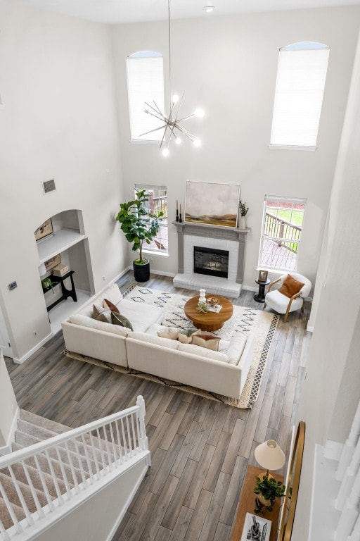 living room with a chandelier, a towering ceiling, wood-type flooring, and a brick fireplace