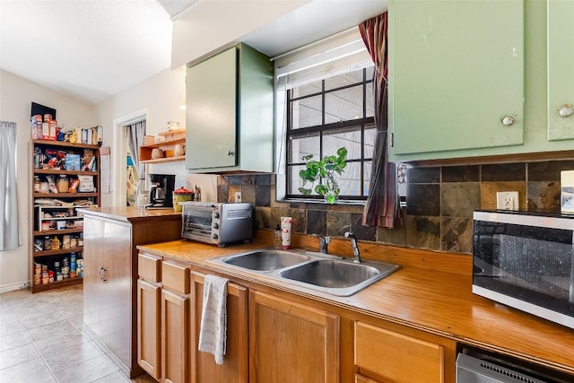 kitchen featuring decorative backsplash, light tile patterned floors, green cabinetry, and sink