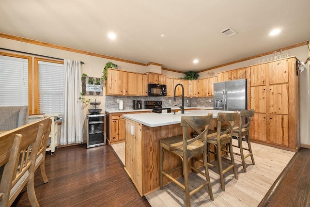 kitchen featuring hardwood / wood-style floors, black appliances, a center island with sink, decorative backsplash, and ornamental molding