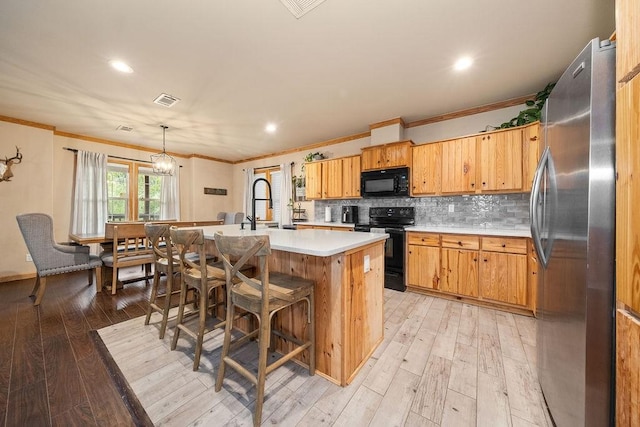 kitchen featuring pendant lighting, an island with sink, ornamental molding, and black appliances