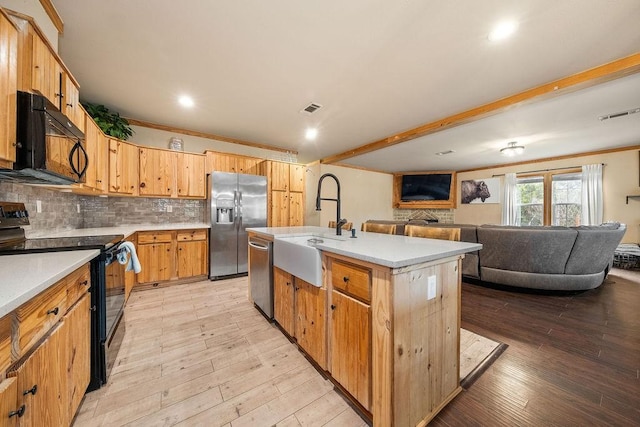 kitchen with black appliances, a center island with sink, sink, decorative backsplash, and beam ceiling